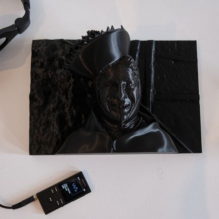 Close-up of a black tactile 2.5D photograph on a white surface, with headphones and an audio device placed nearby.