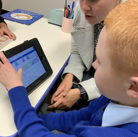 A young boy in a blue shirt working with an OT to use an AAC device