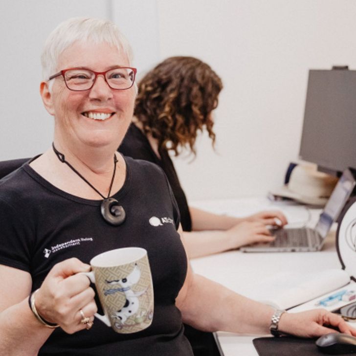 A smiling lady at a computer in a black shirt holding a mug