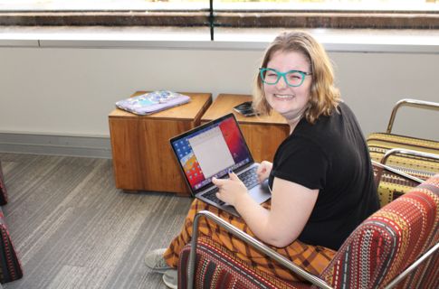 A young woman with a big smile sits on a chair using a laptop