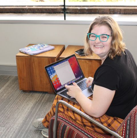 A young woman with a big smile sits on a chair using a laptop