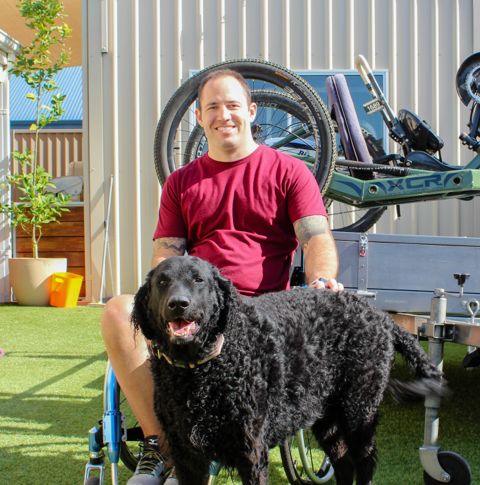 Chris sitting outdoors smiling with his dog.