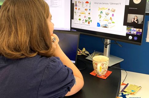 A young woman with short brown hair is watching a computer screen with a presentation playing