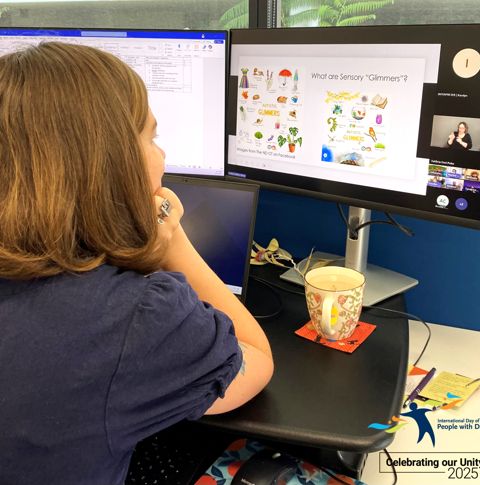 A young woman with short brown hair is watching a computer screen with a presentation playing