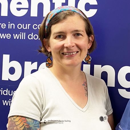 A young woman with short brown hair held back with a headband, wearing a white top with the AT Chat logo in black