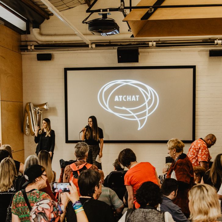 AT Chat Launch - two speakers in front of an audience with the AT Chat logo in the background