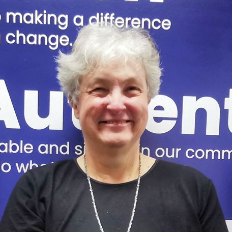 A smiling silver haired older woman wearing a black top and a silver necklace