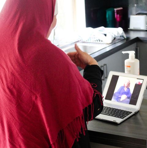 A woman wearing a red hijab facing away from the camera looking at a laptop