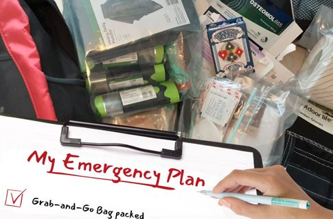 Clipboard with checklist titled 'My Emergency Plan e being held over some supplies including medication, playing cards and gloves