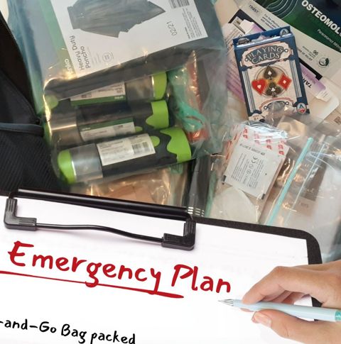 Clipboard with checklist titled 'My Emergency Plan e being held over some supplies including medication, playing cards and gloves