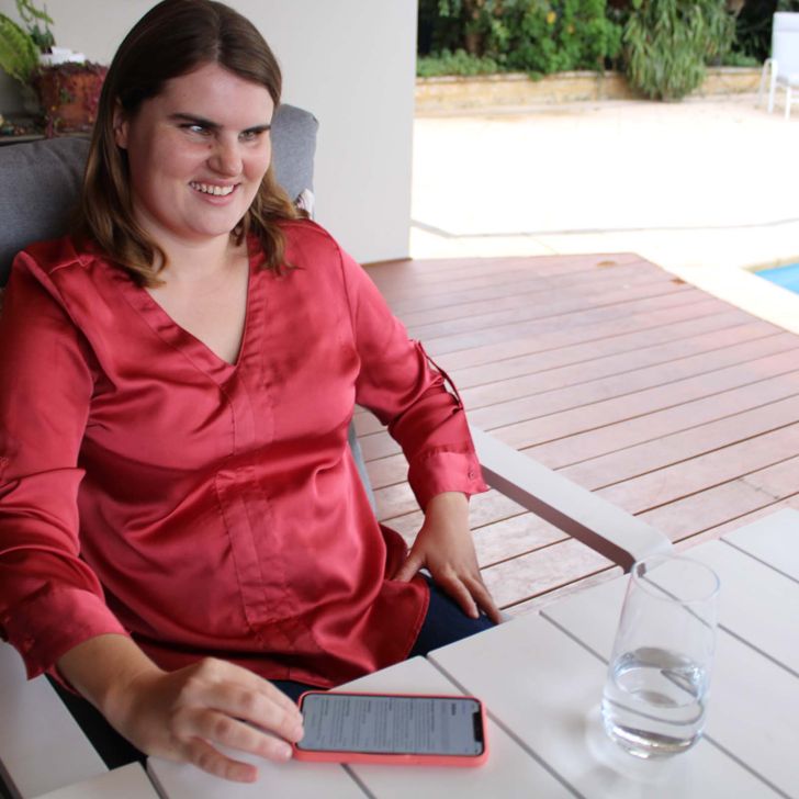 Emma sitting on patio chair with mobile and glass of water