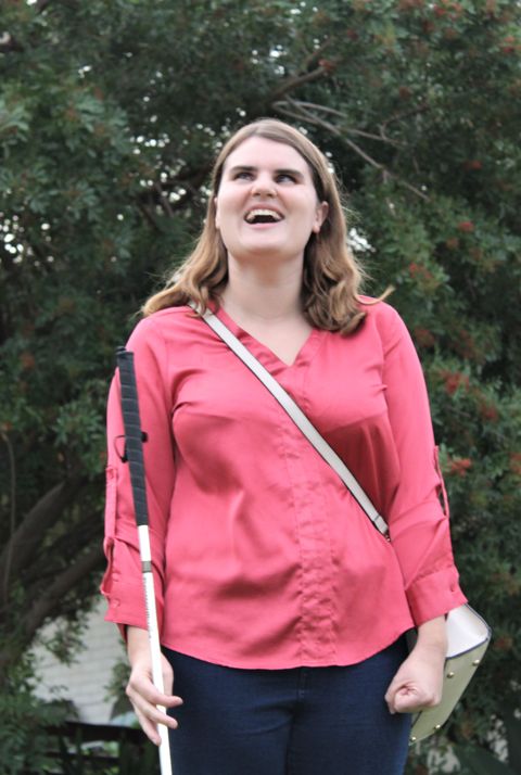 A smiling young woman with a white cane