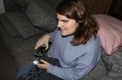 Emma seated on her bed with an iPhone turning a clothing label to audio
