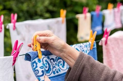 A photo of an older woman's hand clipping a peg to a towel on a clothes line