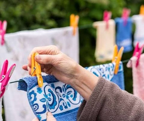A photo of an older woman's hand clipping a peg to a towel on a clothes line
