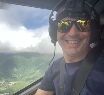 A man in a helicopter with green hills in the background