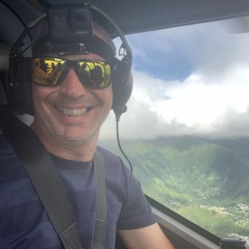 A man in headphones riding a helicopter above green mountains