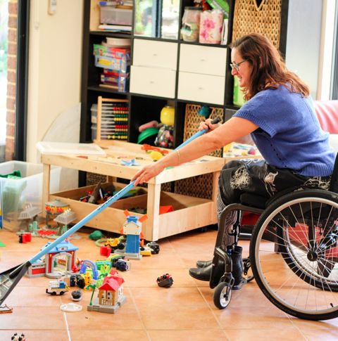 Lisa in living room in her wheelchair cleaning up toys.