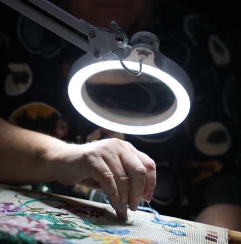 A close-up photo of a woman doing embroidery under an illuminated magnifier