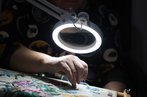 A close-up photo of a woman doing embroidery under an illuminated magnifier