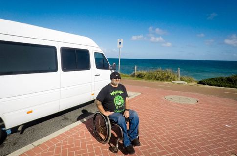 Mark sitting next to the white van on a sunny day at the beach.