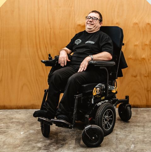 Nick in wheelchair sitting against wooden wall.