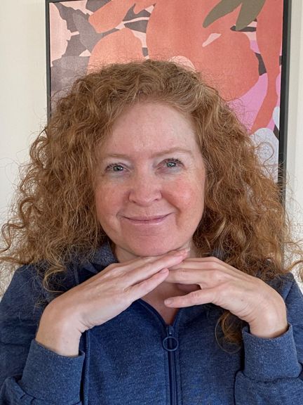 A close up photo of a woman with curly red hair and a kind smile
