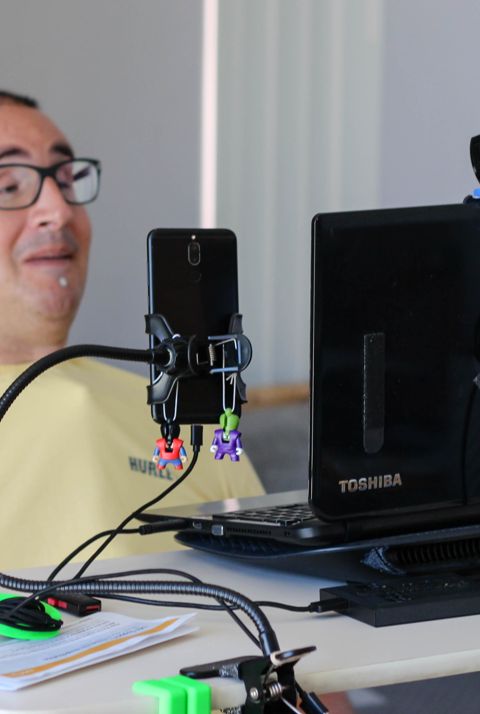 A man in a yellow shirt looking at a computer. Using a head controlled alternative to a computer mouse. 