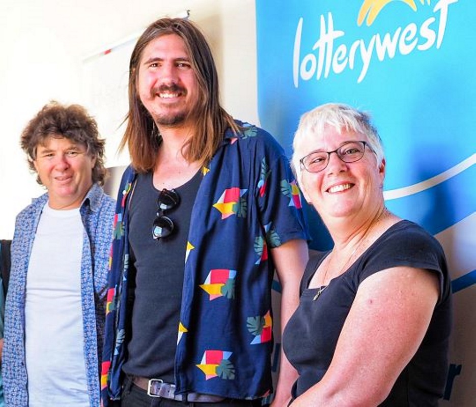 Tony, Lincoln and Gail stand smiling at the camera in front of a Lotterywest banner