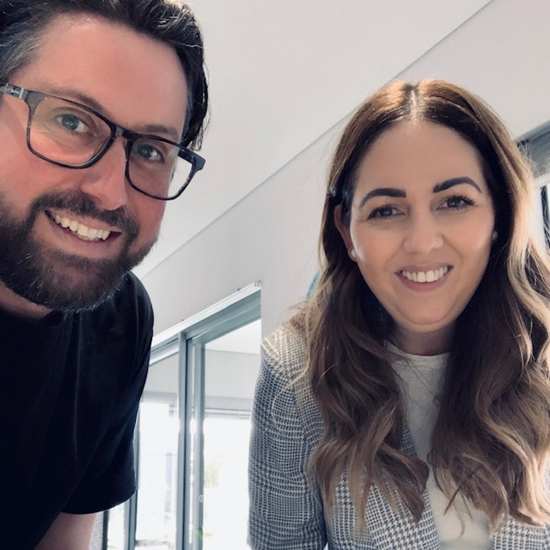 Man and a woman are leaning forward while smiling at the camera