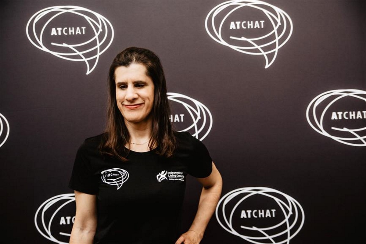 zel_resize woman in black at chat tshirt stands in front of at chat backdrop