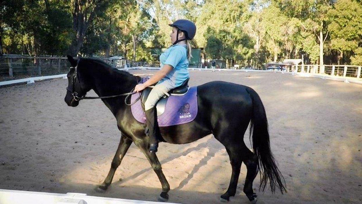 Profile shot of Bec riding her black pony in an outdoor arena. 