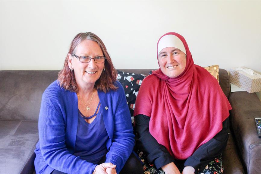 woman wearing red hijab sits next to woman wearing blue top on a couch