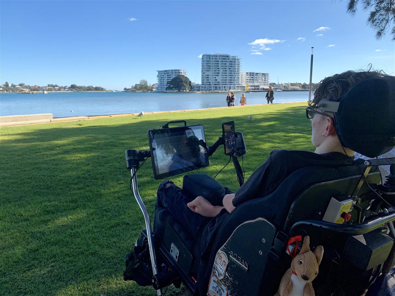 Joey Harrall on the foreshore with his AT A young man seated in his powered wheelchair with his AAC overlooking the Perth foreshore.