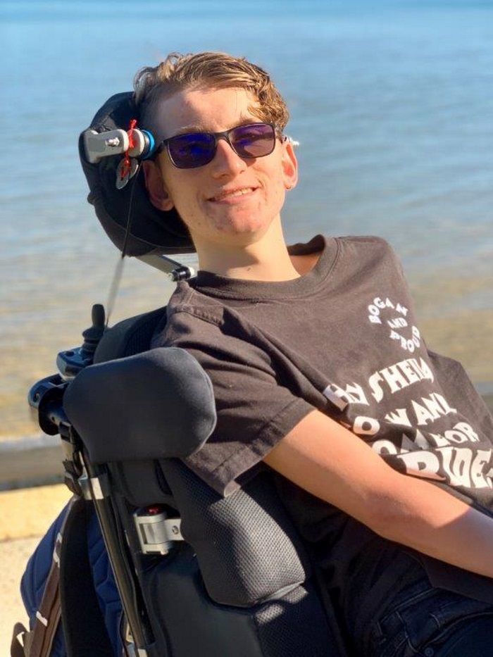 Joey Harrall is seated in his power wheelchair beside the water
