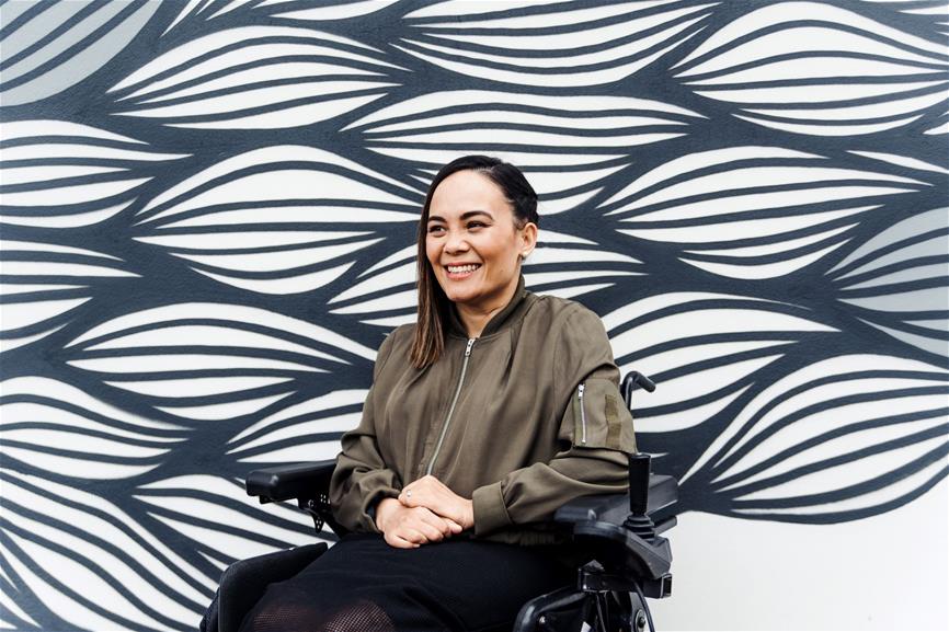 smiling female sits in wheelchair in front of leave like street art