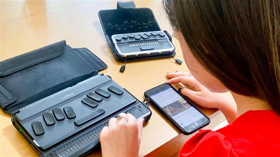 woman wearing red works on her phone and braille note