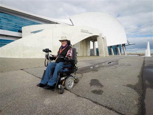 man sits in wheelchair in front of maritime museum