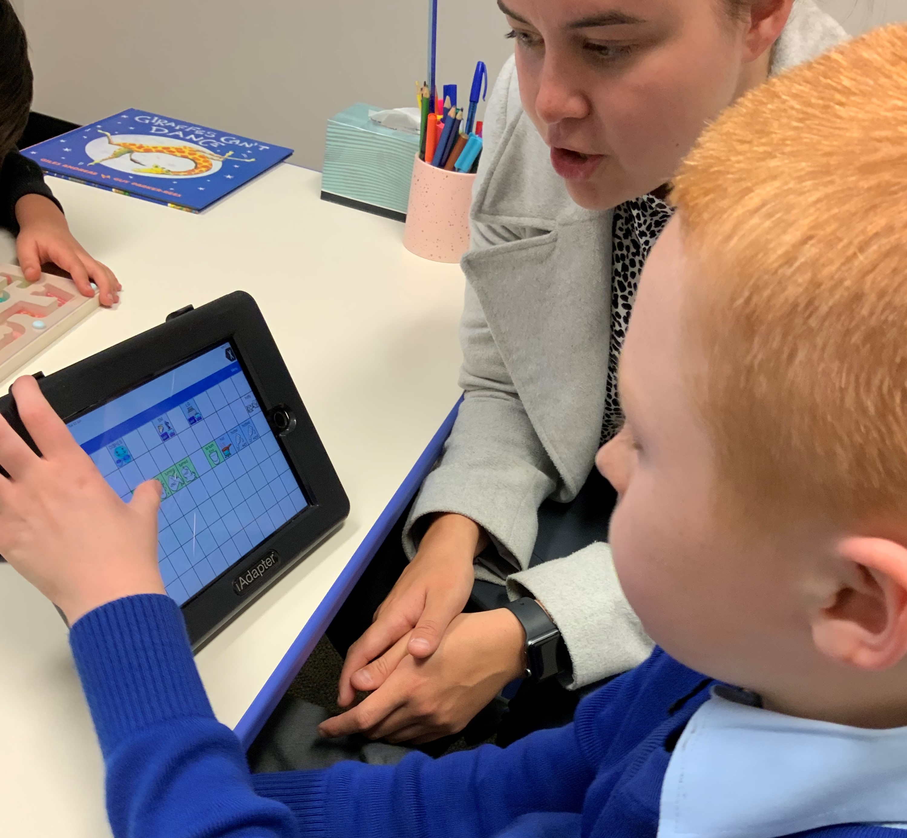 A little boy works with a woman on an AAC device.