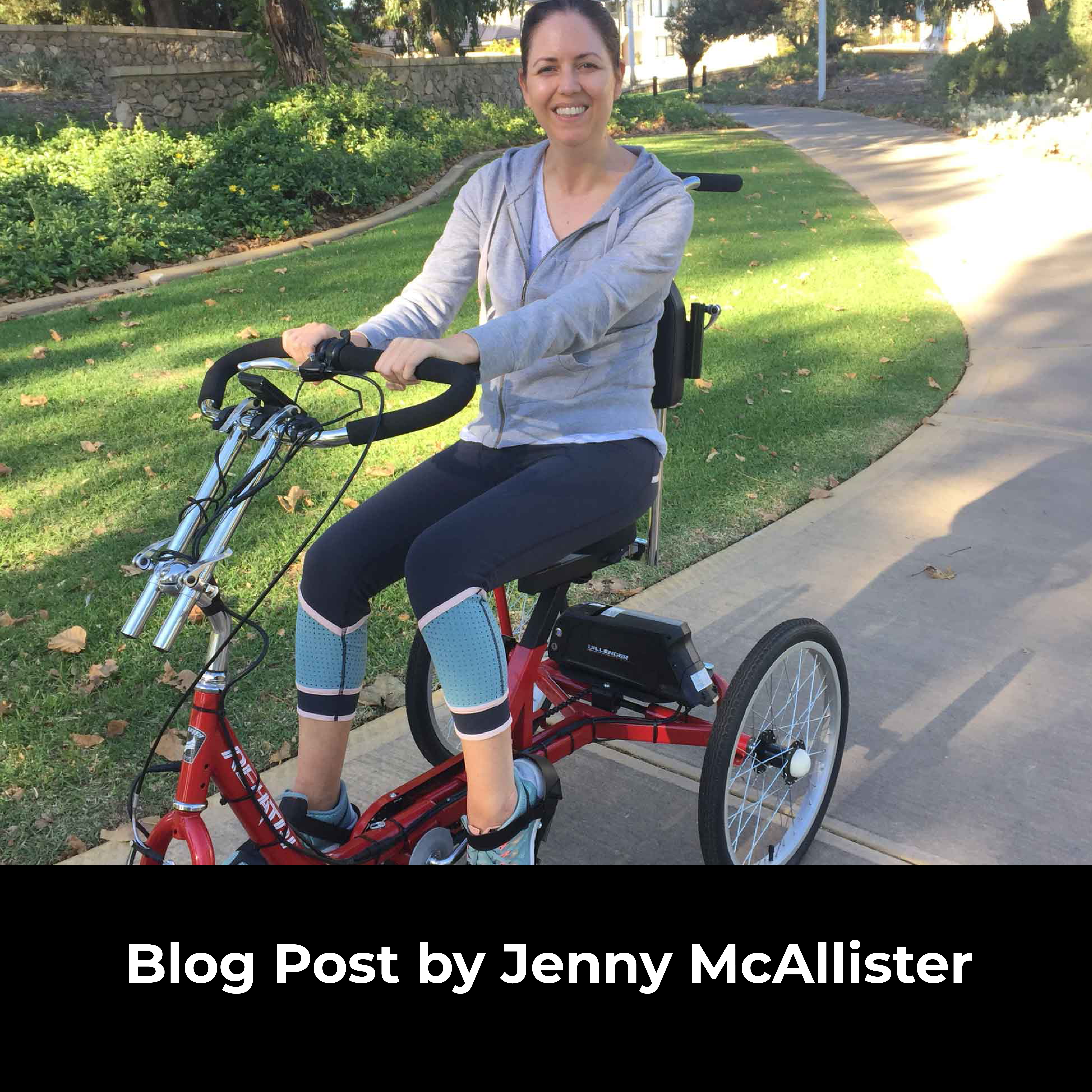 Woman is smiling while seated on her trike in a park like setting.