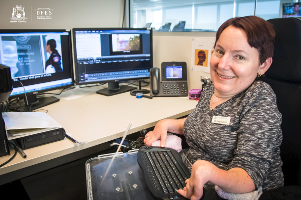 Melanie sits at her modified work station and smiles.