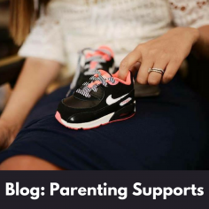 Image of a woman's lap with her finger on a child's pair of black Nike runners.  White text on a black background says, blog: Parenting Supports