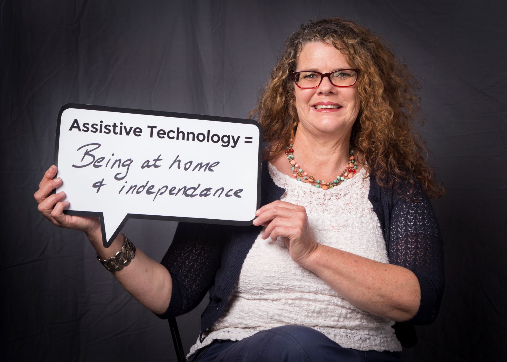 029A9856-1 woman holds speech bubble sign with 'Assistive technology = being at home and independence' written on it'