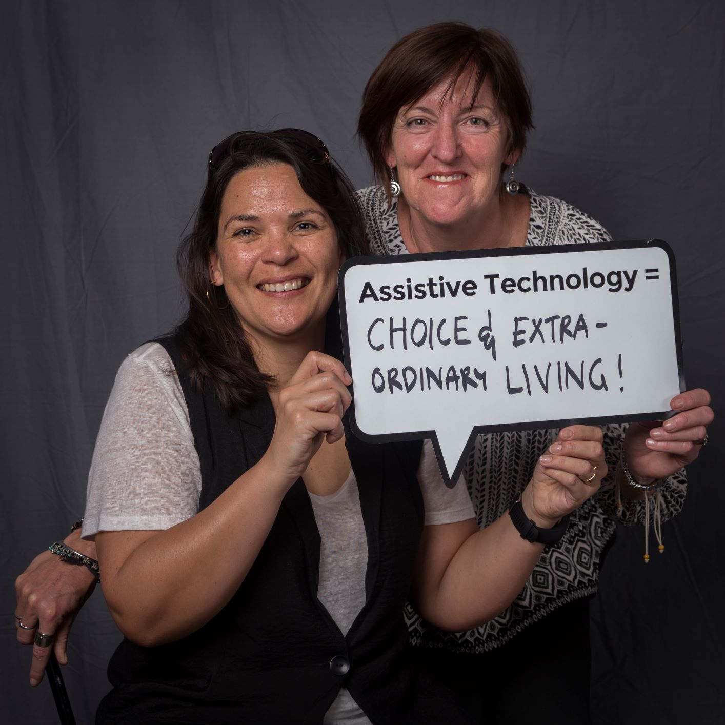 choice two woman holding up a speech bubble sign that reads assistive technology = choice and extra ordinary living