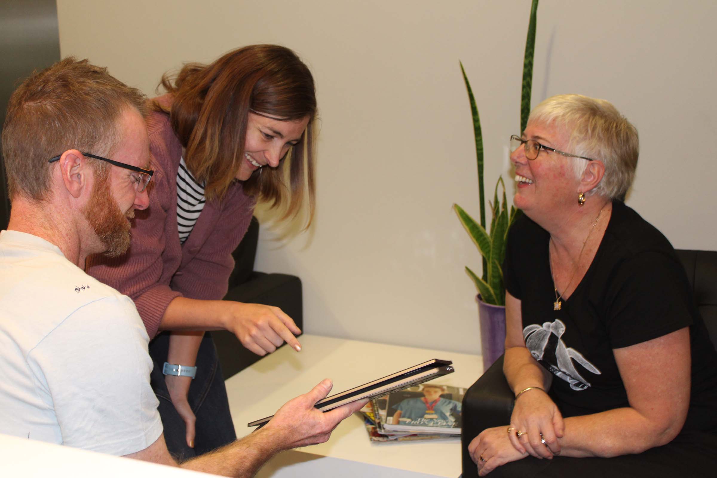 A group of people working together, look at a tablet and smile. A group of people working together, look at a tablet and smile.