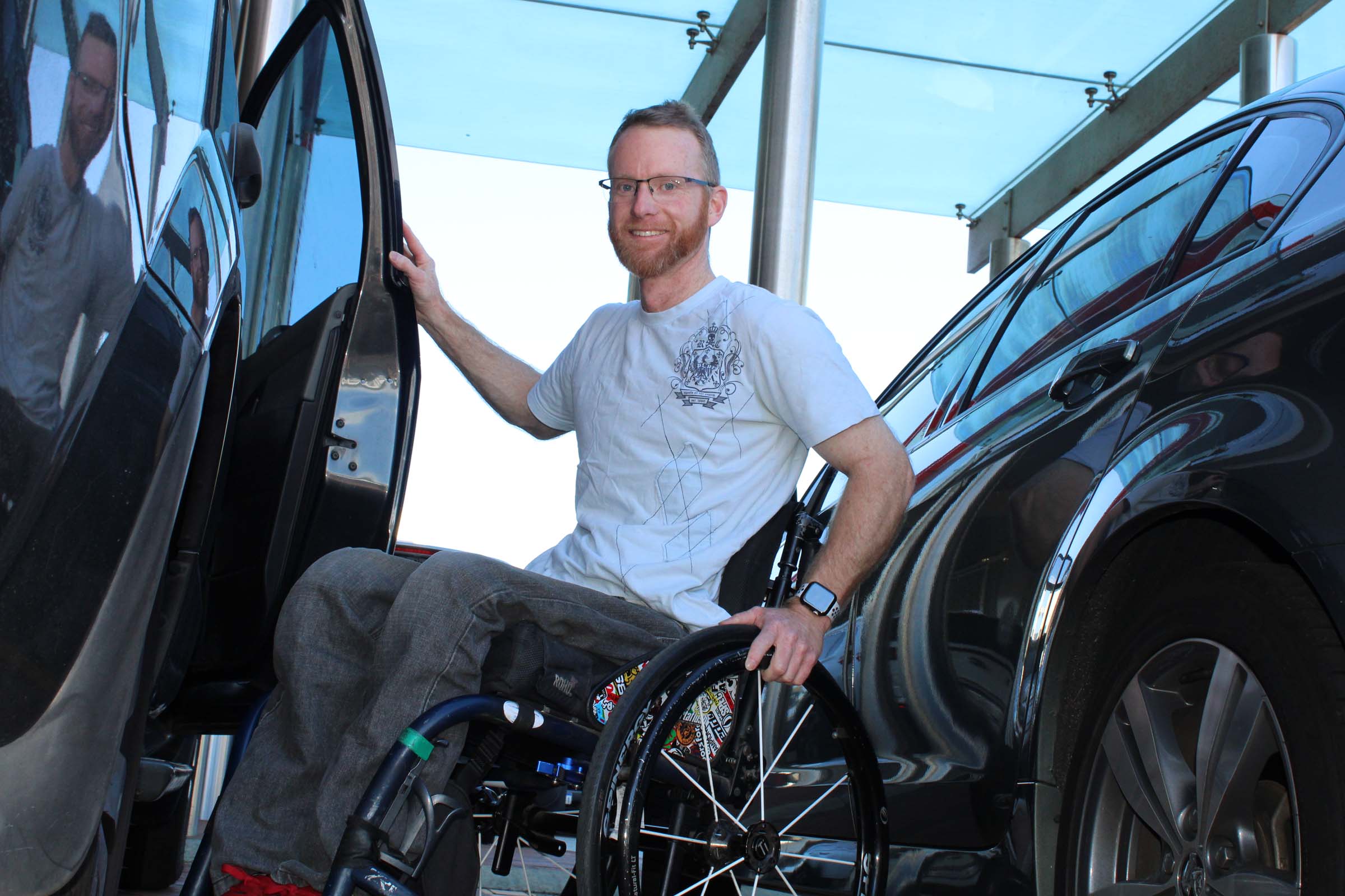 A man sits in a wheelchair with his hand on the car door.