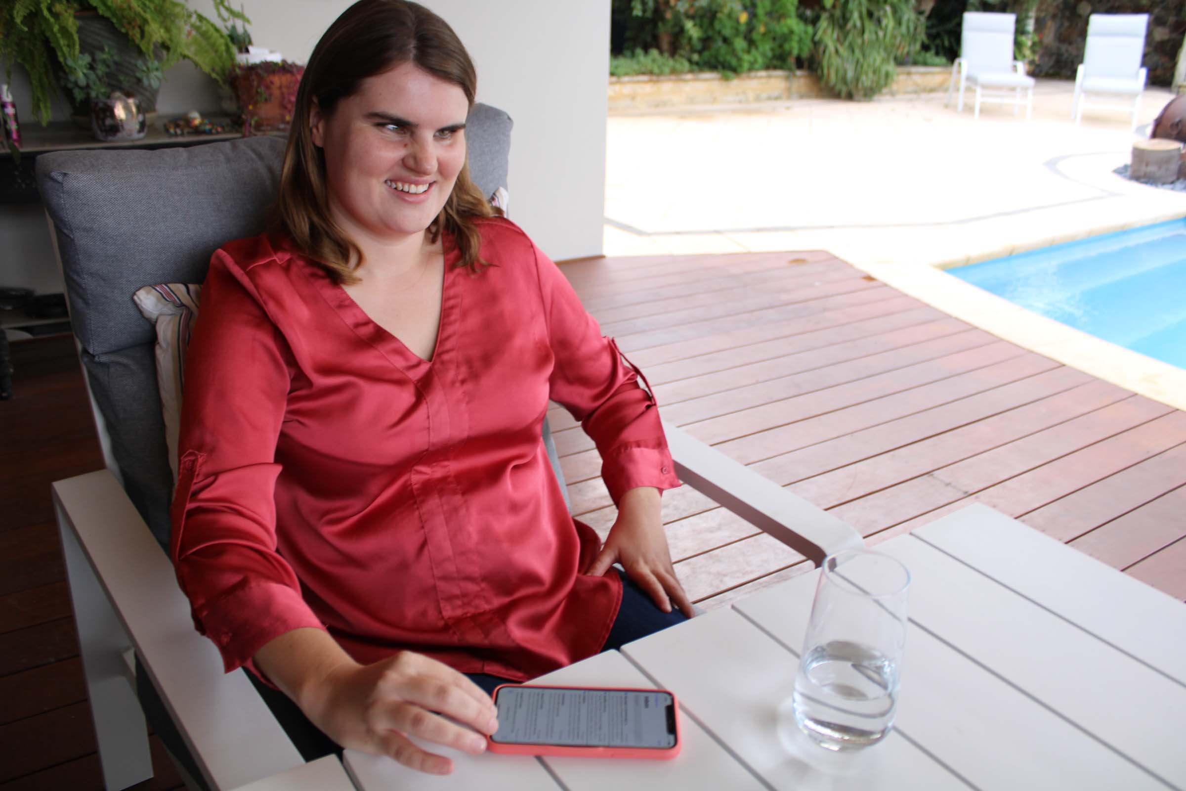 A woman sits at the table and touches a smart phone and smiles.