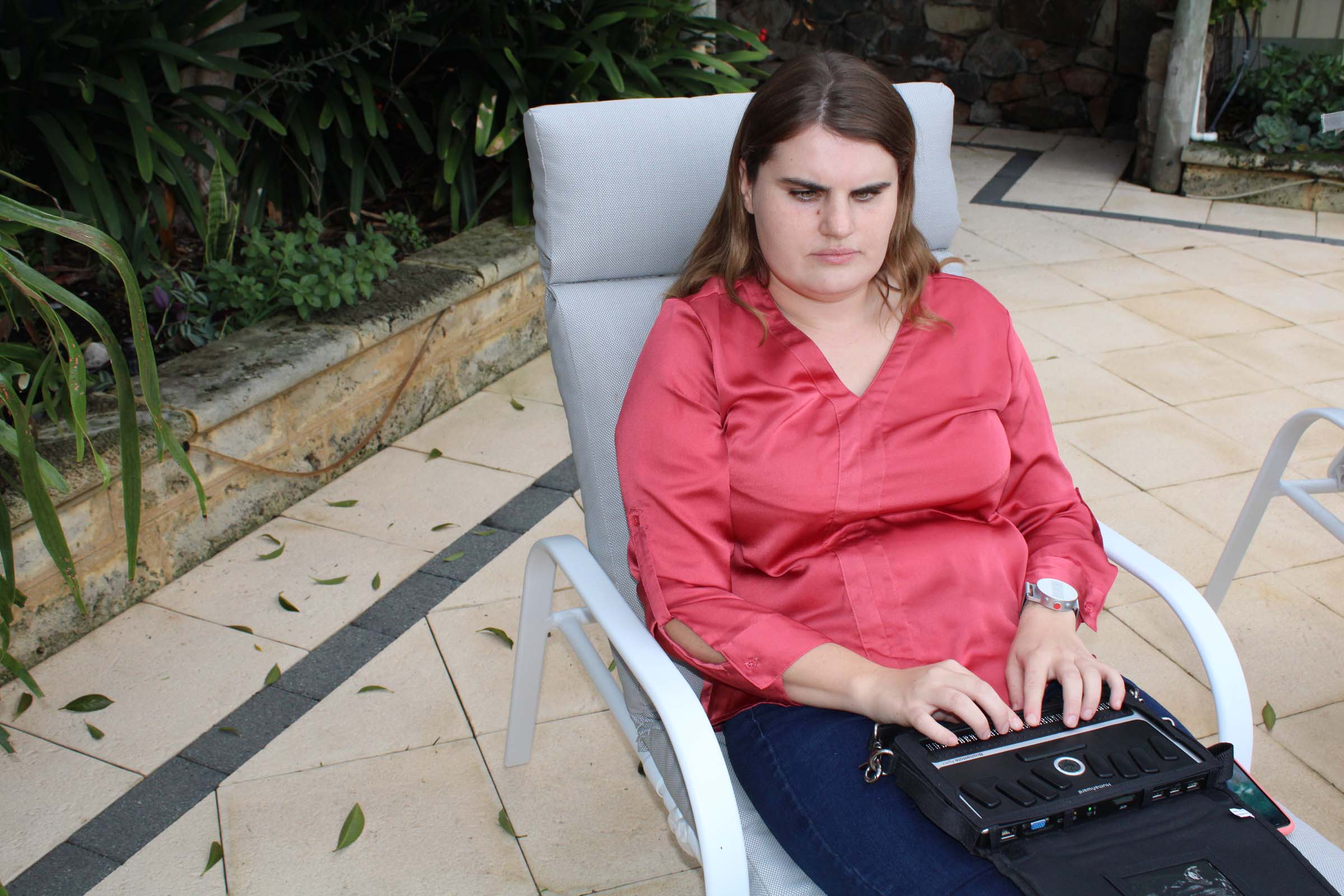 A woman sits on a deckchair and types on her Braille note device.