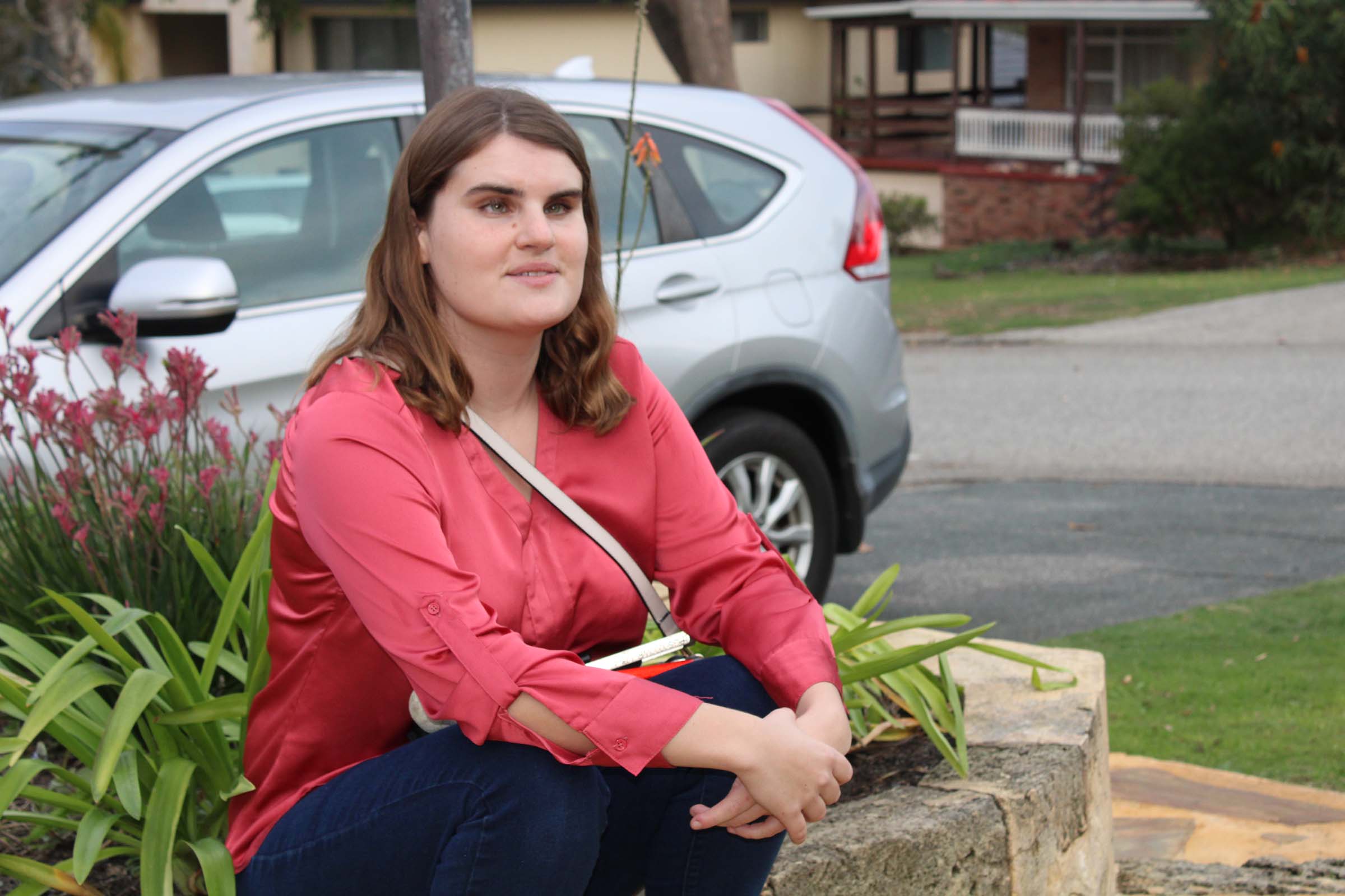 A woman waits with her arms crossed and her white cane in her lap.