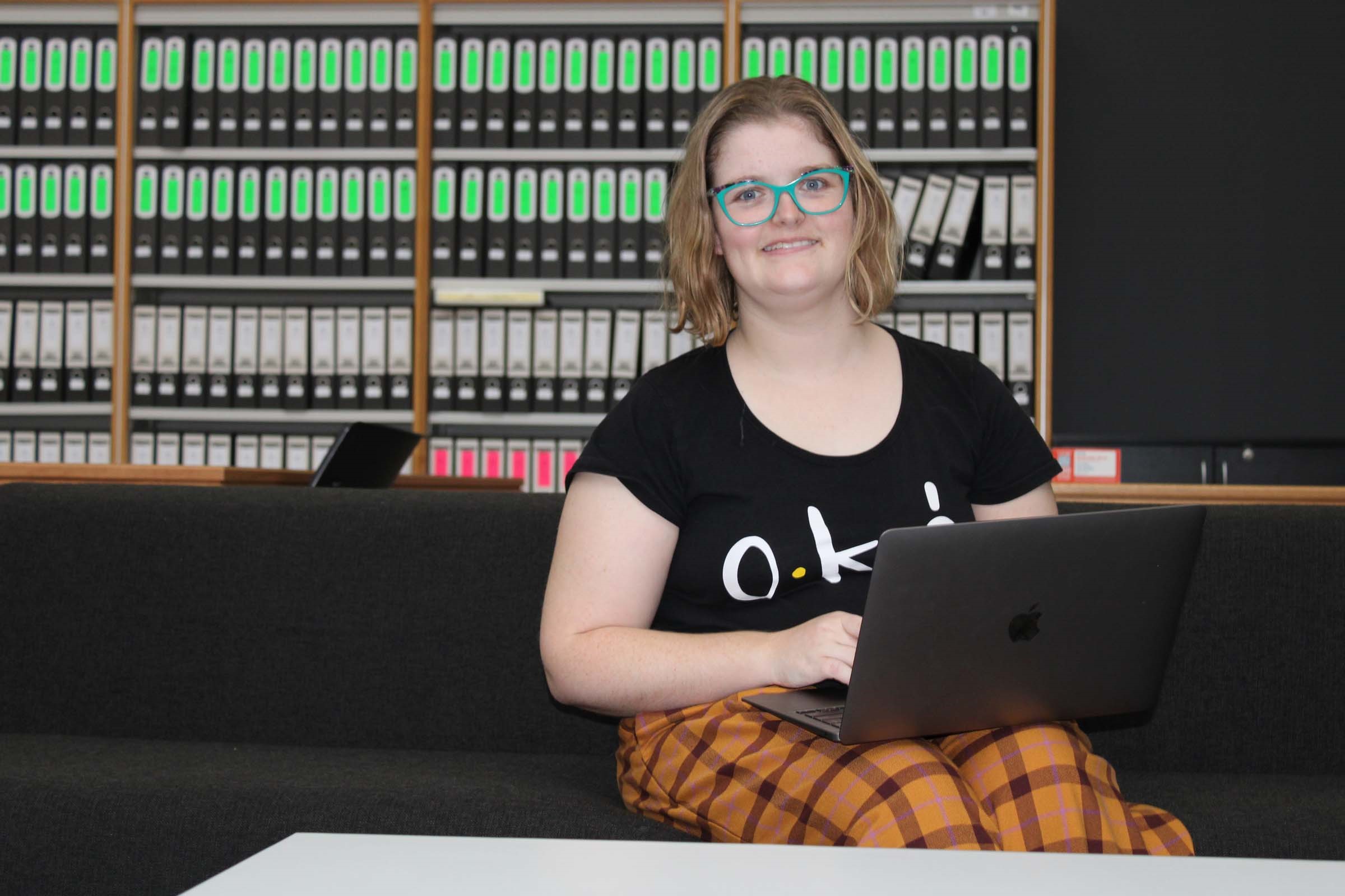 A lady sits at a computer and smiles brightly.